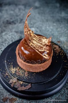 a chocolate dessert on a black plate topped with gold flakes and garnishes