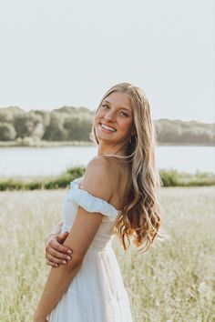 a woman in a white dress standing in a field with her arms around her chest