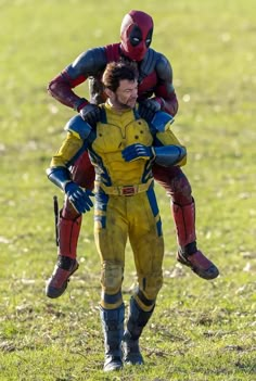 two men in yellow and red suits carrying each other on their back while walking through the grass