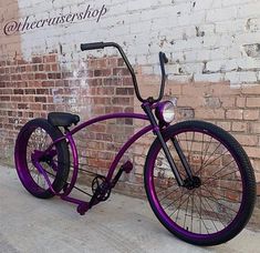 a purple bicycle parked next to a brick wall