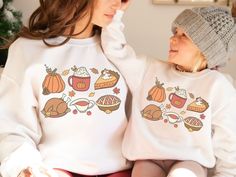 🍂🥧 Feast your eyes on the ultimate festive attire for this Thanksgiving season! Introducing our Matching Mommy and Me Thanksgiving sweaters, perfect for those who want to cozy up in style and celebrate the bounty of the season together. These sweaters come adorned with the most delightful graphic showcasing everyone's favorite Thanksgiving foods - from scrumptious pie to plump pumpkins, a mouth-watering turkey, and let's not forget the rich, creamy gravy! Every glance at these sweaters is a reminder of the delicious feast that Thanksgiving brings. Thinking of making a stylish statement at the family gathering? Our Mommy And Me Outfit ensures that both you and your little one are the center of attention. Whether you're lounging at home watching the parade, preparing the Thanksgiving feast Festive Long Sleeve Fall Sweatshirt, Festive Cotton Tops For Fall, White Family Matching Sweatshirt For Fall, Fall Graphic Print Sweater As A Gift, White Sweatshirt For Fall Holiday, Fall Graphic Print Sweater Gift, Fall Crewneck Sweatshirt, Thanksgiving Foods, Fall Crewneck