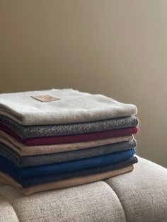 four folded towels stacked on top of each other in different colors and sizes, sitting on a couch