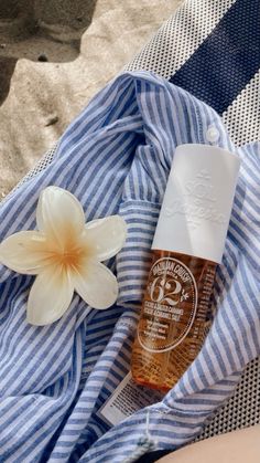 an open bottle of sunscreen next to a flower on a blue and white towel