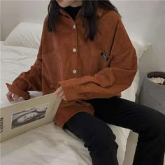 a woman is sitting on a bed and holding an open book in her hands while wearing black pants