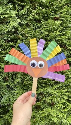 a hand holding a colorful paper turkey on a stick