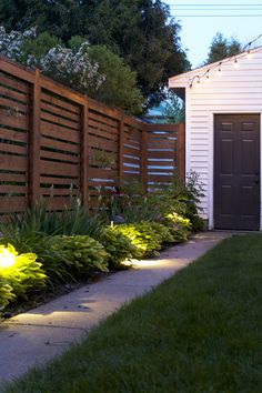 some lights that are on in the grass near a fence and a building with a door