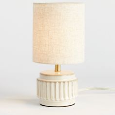 a white ceramic lamp with a beige linen shade on the base and a gold - plated metal light fixture