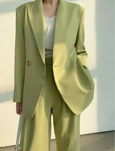 a woman standing in front of a white wall wearing a lime green suit and hat