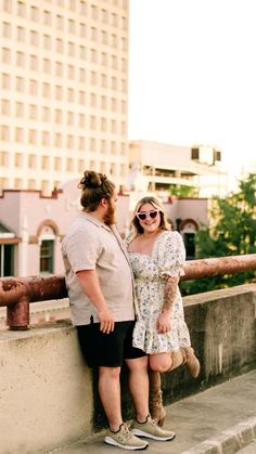 a man and woman standing next to each other on the side of a bridge with buildings in the background