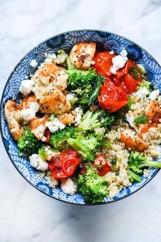 a blue bowl filled with broccoli, tomatoes and cauliflower on top of a marble counter