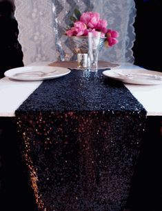 the table is set with two plates and pink flowers in a vase on top of it