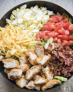 a salad with chicken, lettuce, tomatoes, cheese and bacon in a bowl