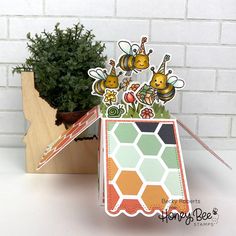 an open card with bees and flowers on it, sitting next to a potted plant