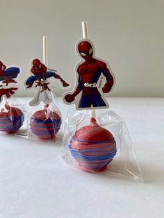 three spiderman lollipops wrapped in cellophane on a white surface