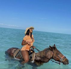 a woman riding on the back of a brown horse in clear blue water with a cowboy hat