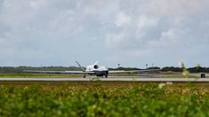 an airplane that is sitting on the runway in front of some bushes and grass,