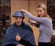 a woman cutting a man's hair with scissors and a helmet on his head