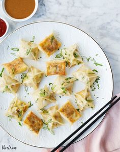 a white plate topped with wontons next to dipping sauce and chopsticks