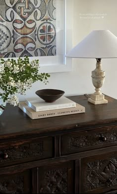 a lamp on top of a wooden dresser next to a vase with flowers and books