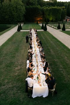 a long table with people sitting at it in the middle of an outdoor garden area