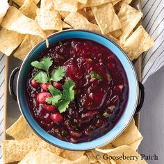 a blue bowl filled with cranberry salsa surrounded by tortilla chips