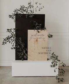 two wooden signs sitting next to each other on top of a white box with plants growing out of it