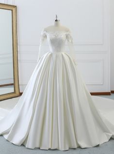 a white wedding dress on display in front of a mirror with a gold framed frame