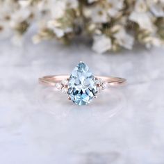 an aqua blue and white diamond ring sitting on top of a table next to flowers