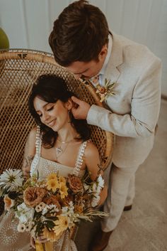 a bride and groom sitting in a wicker chair with flowers on their wedding day