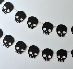 a string of black paper skulls hanging from a line on a white wall with one skull in the middle