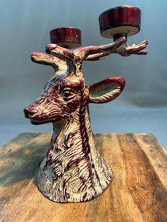 a deer head candle holder with two candles on it's antlers, sitting on top of a wooden table