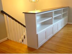 a white entertainment center in the corner of a room with wood flooring and handrails