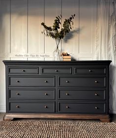 a black dresser with gold knobs and flowers on top, against a white wall