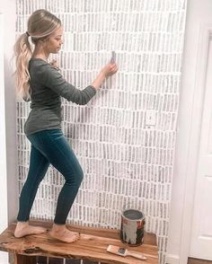 a woman standing on top of a wooden shelf next to a wall covered in newspaper strips