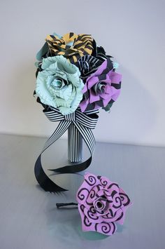 an origami flower bouquet with ribbon tied around it on a table next to a paper heart