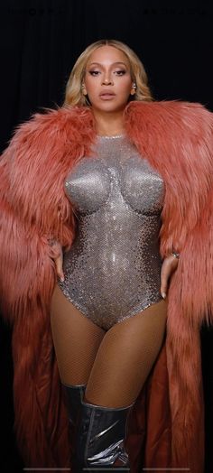 a woman in a silver bodysuit and fur coat posing for the camera with her hands on her hips