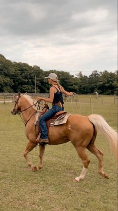 a woman riding on the back of a brown horse across a lush green field with trees in the background