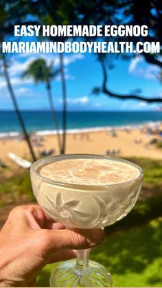 a person holding up a wine glass in front of an ocean and palm tree line