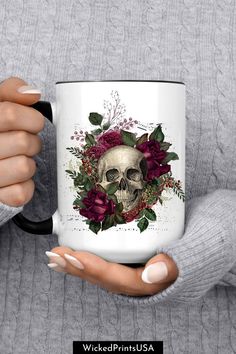 a woman holding a white coffee mug with a skull and flowers on the front in her hands