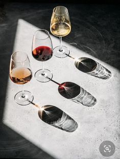 four wine glasses with different wines in them on a white table top, one is empty and the other half has been partially filled