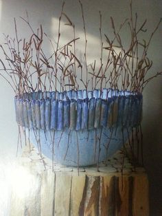 a blue planter sitting on top of a wooden table next to a wall with dry grass growing in it