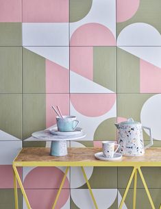 a wooden table topped with cups and saucers next to a wall covered in geometric tiles