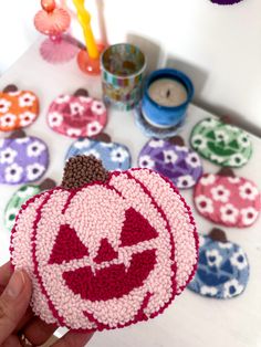 a person holding up a knitted pumpkin ornament on top of a table