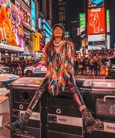 a woman sitting on top of a trash can in the middle of a busy street