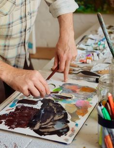 a man is painting on an easel with paintbrushes