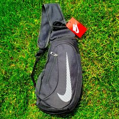 a nike backpack laying on the grass with a tag in it's pocket next to its strap