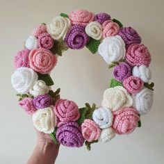 a hand holding a crocheted wreath with pink, white and purple flowers on it