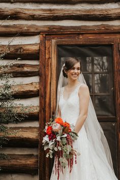 a bride standing in front of a log cabin holding her bouquet