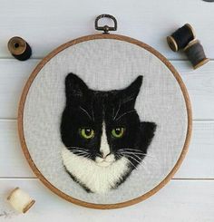 a black and white cat with green eyes in a hoop next to some spools of thread