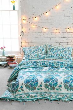 a bed with blue and white bedspread in front of a brick wall decorated with string lights